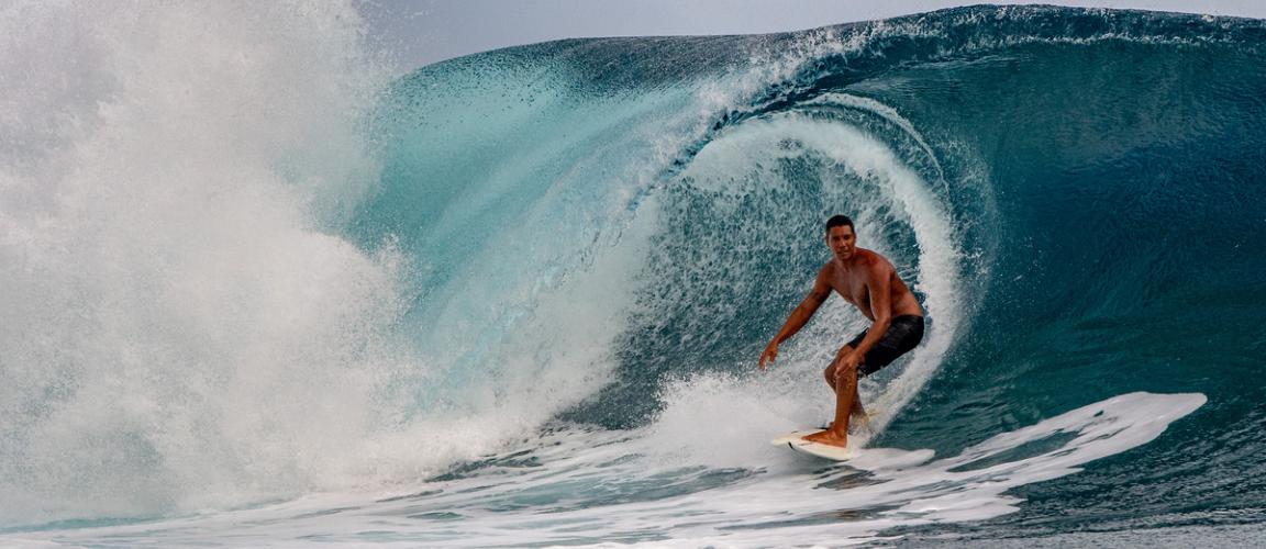 Tanned male surfer riding a wave on a white surf board
