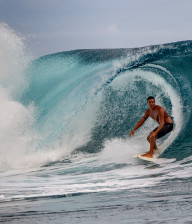 Tanned male surfer riding a wave on a white surf board