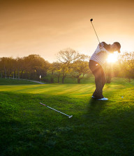 Man in cap chipping on to a golf green at sunset