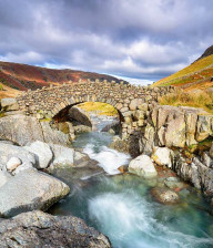 Dry stone wall bridge over a stream with rocky, heather clad banks.