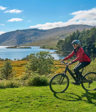 A cyclist riding through Lough Shore Park with sunlight on loch in background