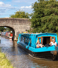 Canal boat floating along Cheshire Canal with bridge in background