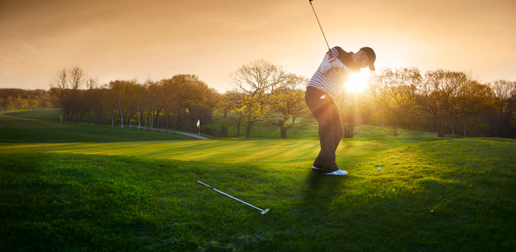 A man plating Golf at sunset with green grass and autumn trees