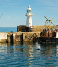 Man reeling in a fish off a small harbour with a small fishing boat nearby