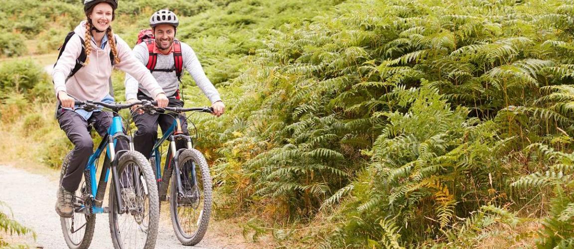 A man and a woman cycling along a mountain bike trail with ferns either side