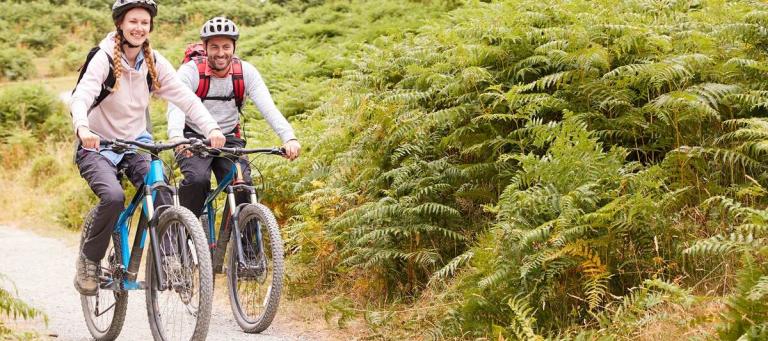 A man and a woman cycling along a mountain bike trail with ferns either side