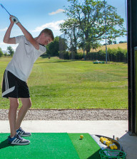 Boy teeing off in covered bay at driving range