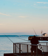 Two men fishing off Penarth Pier with large expanses of pink skies and blue water