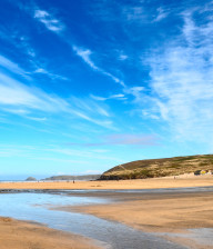 Wide view of sand and sea at Perranporth beach with beach bar in background