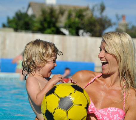 Blonde woman and child with football laughing in a swimming pool