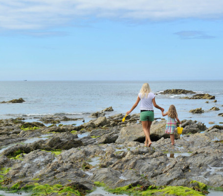 Blonde woman and small girl exploring rock pools in Cornwall