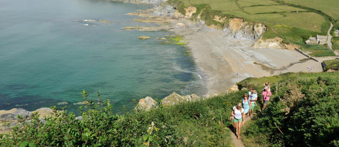 Group of people walking the coastal path above a sandy beach in Cornwall