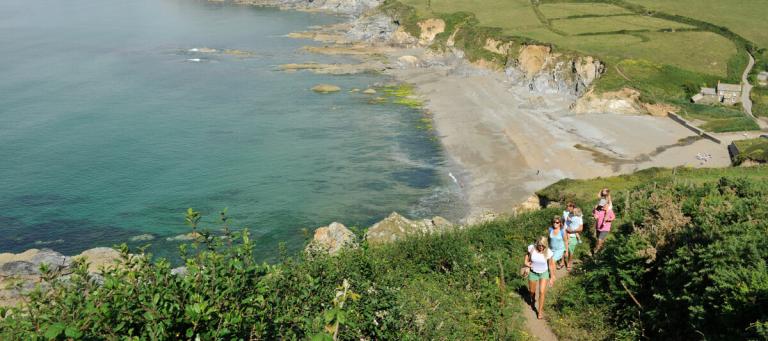 Group of people walking the coastal path above a sandy beach in Cornwall