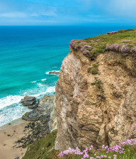 Rocky cliff with wildflowers and waves breaking on the beach below